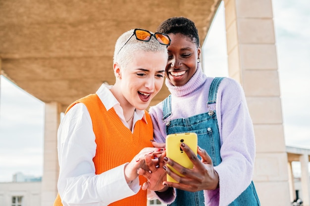 Duas lindas meninas se divertindo usando o aplicativo em um telefone inteligente Um par de amigos procurando ofertas na internet