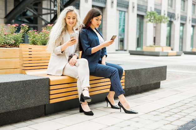 Duas lindas moças de terno com telefones celulares