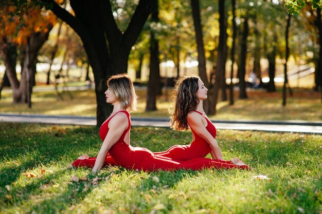 Duas lindas mulheres adultas praticam esportes sentadas em esteiras no parque de verão