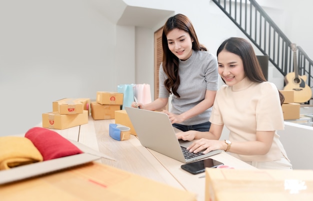 Duas lindas mulheres asiáticas conferem os pedidos em laptops pela internet.