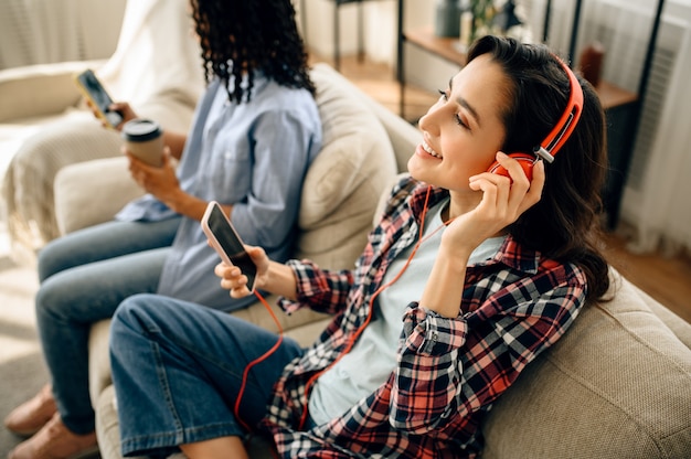 Duas lindas mulheres com fones de ouvido relaxando no sofá