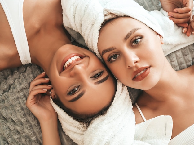 Foto duas lindas mulheres sorridentes com roupões de banho brancos e toalhas na cabeça