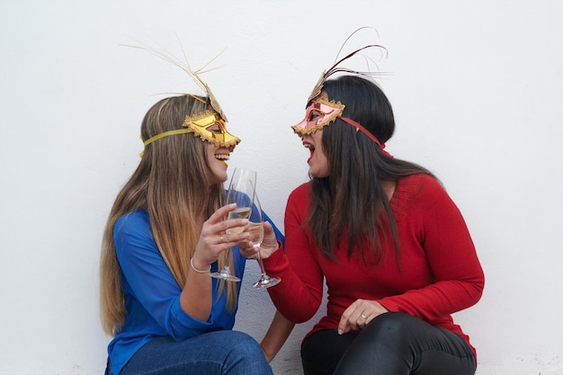 Foto duas lindas mulheres usando máscaras de carnaval venezianas riem junto com uma bebida nas mãos