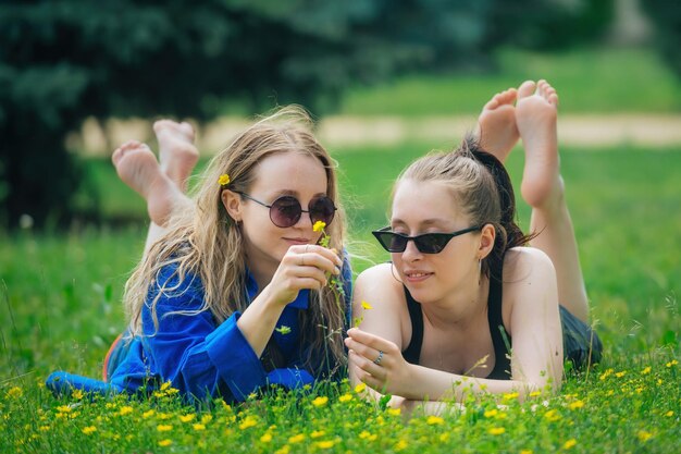 Duas lindas namoradas felizes deitam-se num prado verde brilhante com flores amarelas