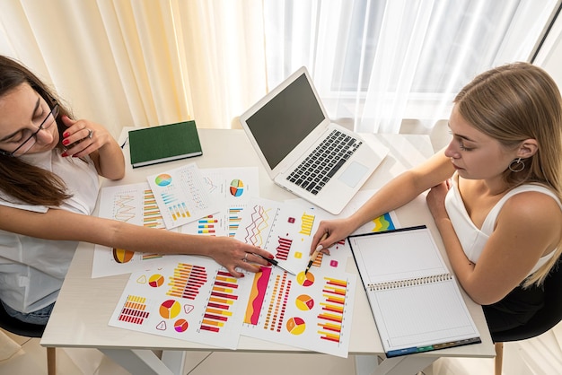 Duas lindas super mulheres de negócios olhando para gráficos de cores no trabalho. Conceito de gráfico