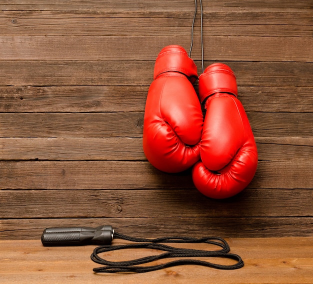 Duas luvas de boxe vermelhas penduradas em um fundo marrom de madeira