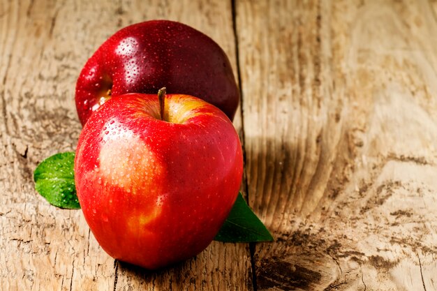 Duas maçãs vermelhas com gotas de água em uma mesa de madeira