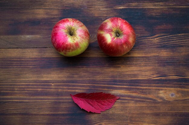 Duas maçãs vermelhas e folhas de outono no fundo de madeira