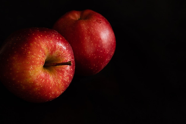 Duas maçãs vermelhas frescas maduras com gotas de água na casca brilhante na superfície preta