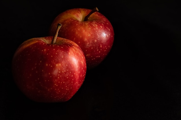 Duas maçãs vermelhas frescas maduras com gotas de água na casca brilhante na superfície preta