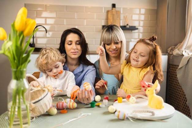 Duas mães felizes com seus filhos decoram ovos de páscoa