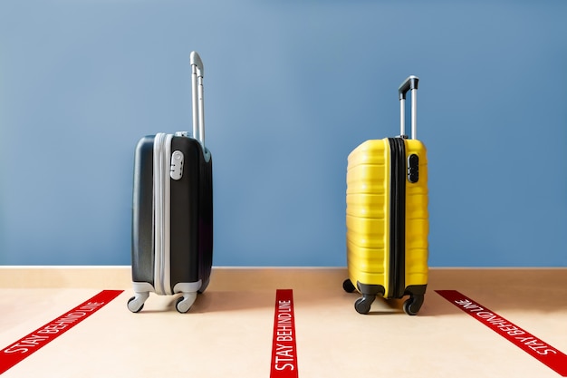 Duas malas de viagem uma preta e uma amarela esperando na fila para continuar há uma marca vermelha no chão