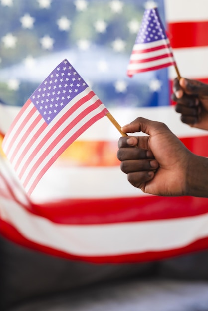 Duas mãos agitam pequenas bandeiras americanas contra um fundo desfocado.