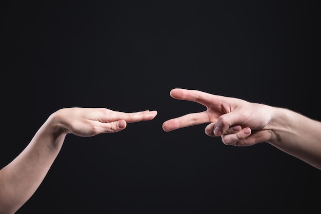 Duas mãos caucasianas mostrando tesouras e gestos de papel em fundo preto