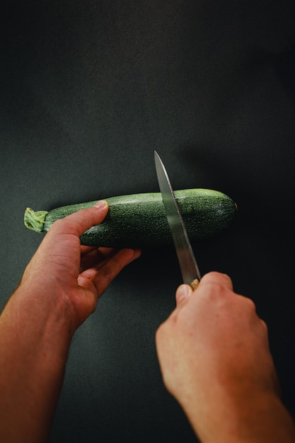 Duas mãos cortando um pepino com uma faca comprida