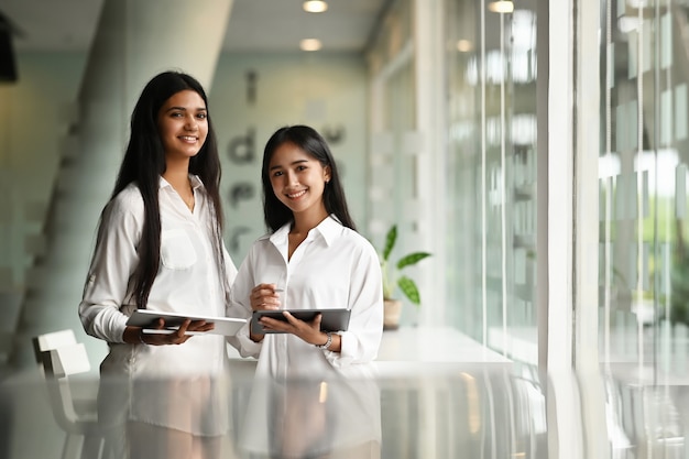 Duas mãos de jovem empresária segurando um tablet em um escritório moderno.