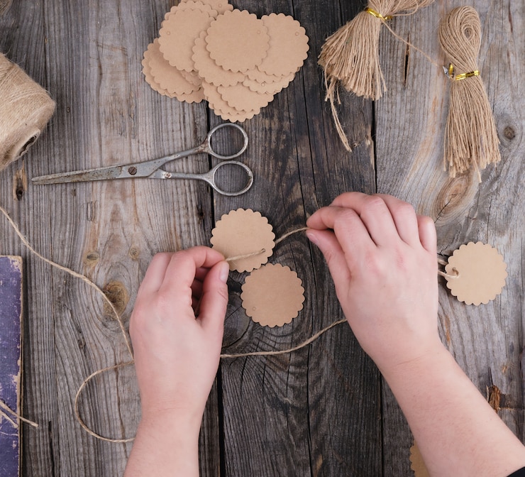 Foto duas mãos femininas e etiquetas de papel com uma corda marrom em uma mesa de madeira cinza