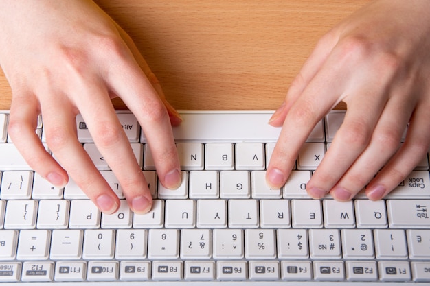 Foto duas mãos femininas está digitando em um teclado branco com letras em inglês, close-up, foco seletivo. o conceito de ensino em casa, ensino à distância