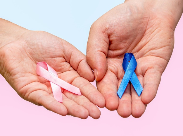 Duas mãos segurando duas fitas rosa e azul para as campanhas de Outubro Rosa e Novembro Azul