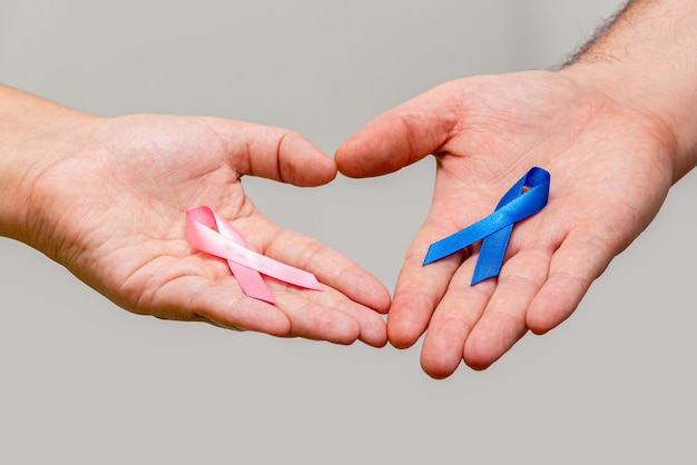 Duas mãos segurando duas fitas rosa e azul para as campanhas Pink October e Blue November para apoiar a vida e aumentar a conscientização sobre o câncer Mão do homem e mão da mulher