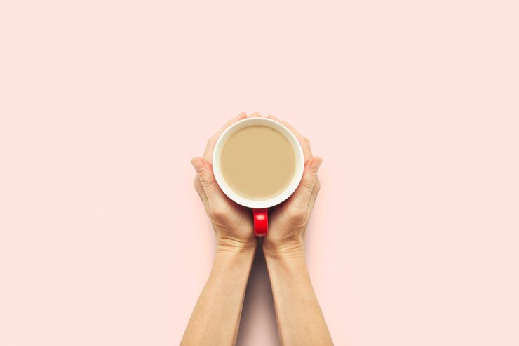 Foto duas mãos segurando uma xícara com café quente em um fundo rosa. conceito de café da manhã com café ou chá. bom dia, noite, insônia. vista plana, vista superior