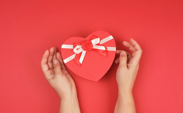 Duas mãos segurar um papel fechado caixa vermelha em forma de um coração