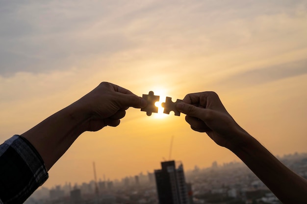 Duas mãos tentando conectar peça de quebra-cabeça de casal com fundo por do sol Quebra-cabeça de madeira sozinho contra raios solares uma parte de todo o símbolo de estratégia de negócios de associação e conexão