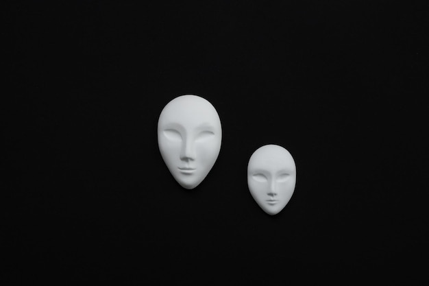 Foto duas máscaras de gesso branco de humanos com olhos fechados em fundo preto