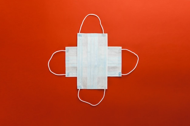 Duas máscaras protetoras médicas respiratórias encontram-se na forma de uma cruz sobre um fundo vermelho.