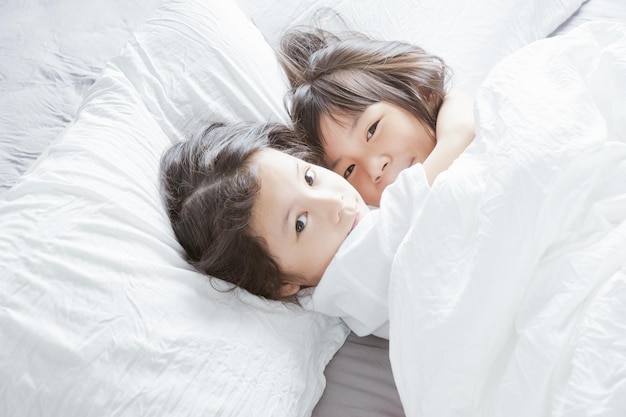 Duas menina chinesa asiática abraçam-se e deitam-se na cama