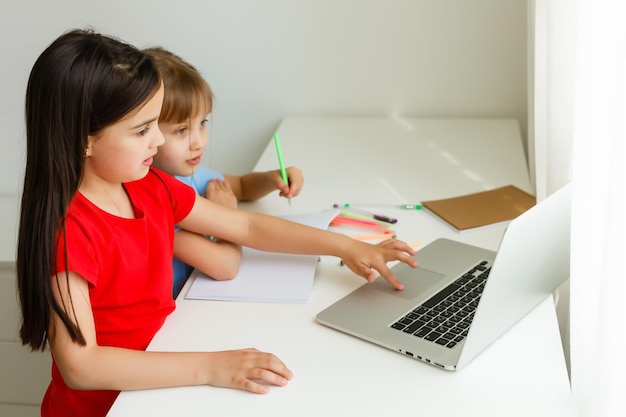 Duas meninas, a mais velha e a mais nova, estão ocupadas em uma mesa em um laptop.