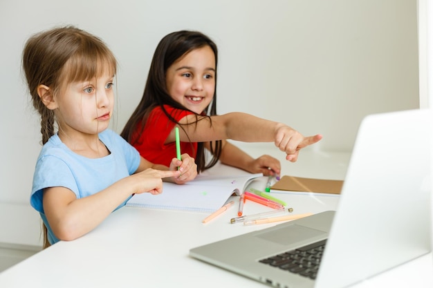 Duas meninas, a mais velha e a mais nova, estão ocupadas em uma mesa em um laptop.