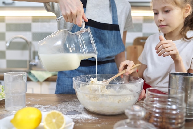 Duas meninas, adolescente e irmã mais nova, preparando biscoitos juntos na cozinha. As crianças misturam a farinha na tigela, despeje o leite na massa. Família, amizade, diversão, comida caseira saudável