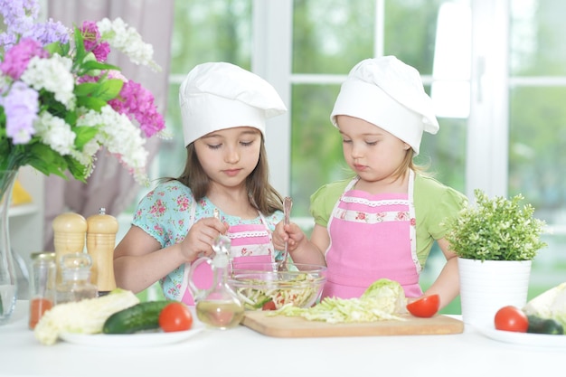 Duas meninas adoráveis em aventais preparando uma deliciosa salada