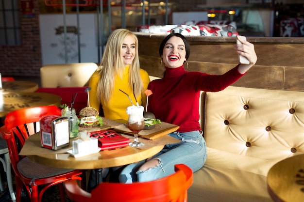 Duas meninas alegres alegres, tomando uma selfie enquanto sentados juntos no café