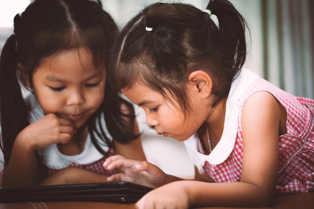 Duas meninas asiáticas divertindo-se assistindo vídeos em um tablet.