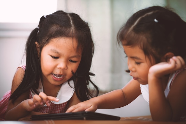 Duas meninas asiáticas divertindo-se assistindo vídeos em um tablet.