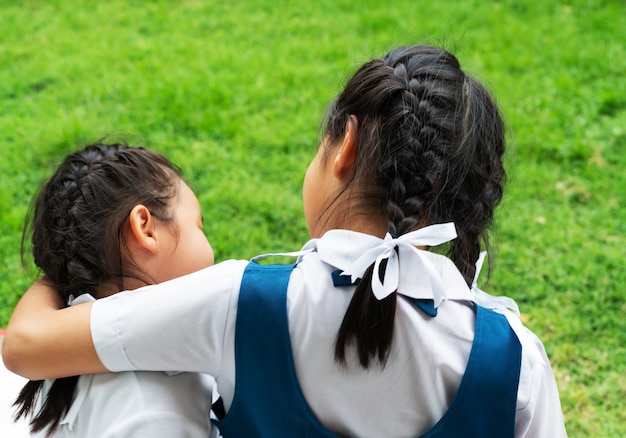 Duas meninas asiáticas irmãs abraçando feliz post na escola uniforme, volta ao conceito de escola