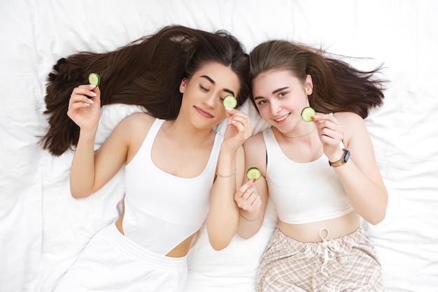 Duas meninas bonitas com fatias de pepino para os olhos mulheres fazem máscaras para cuidar de sua pele amigas no spa em casa descansam e relaxam