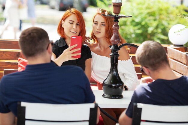 Foto duas meninas bonitas fumam narguilé em um café em um dia de verão no terraço
