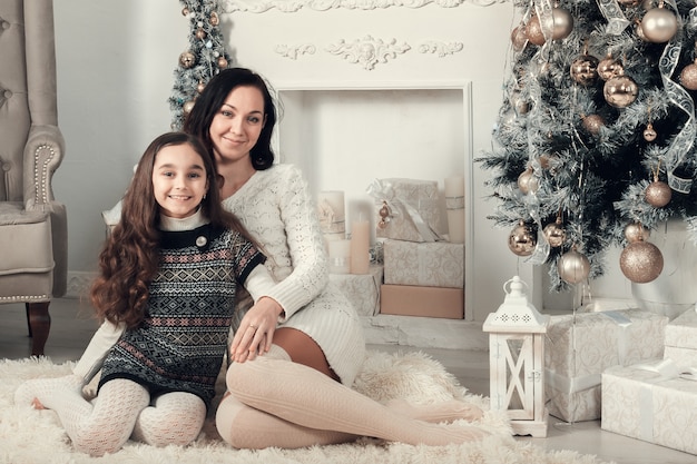 Duas meninas bonitas, mãe e filha, localização no chão no quarto decorado de Natal.