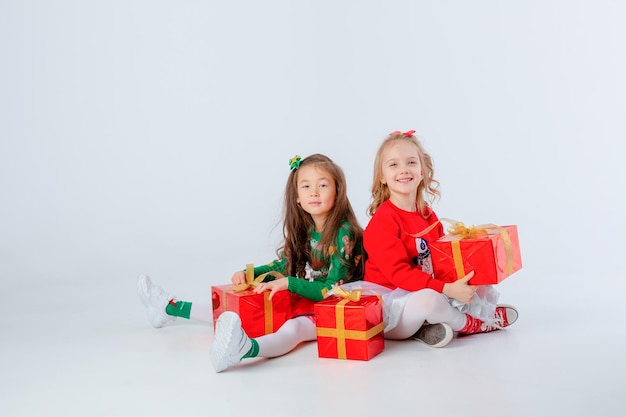 Duas meninas bonitinhas de suéter vermelho, caixa de presente sentada fundo branco conceito de natal espaço de texto