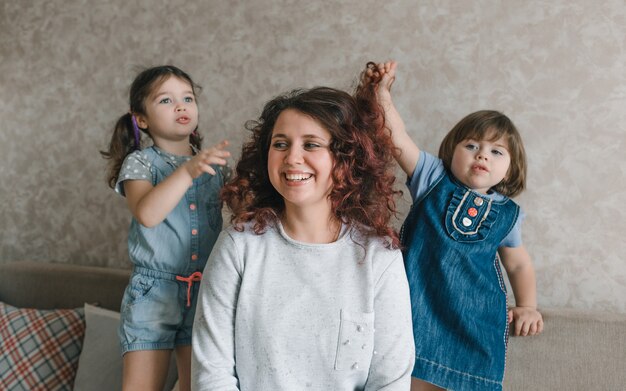 Duas meninas brincam com a mãe, arrumam, penteiam seus cabelos. mãe feliz e alegre