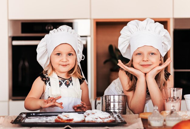 Duas meninas com chapéus brancos de chef se divertem juntas na cozinha