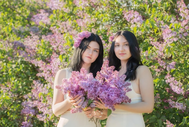 Duas meninas com lilás florescendo na luz do sol