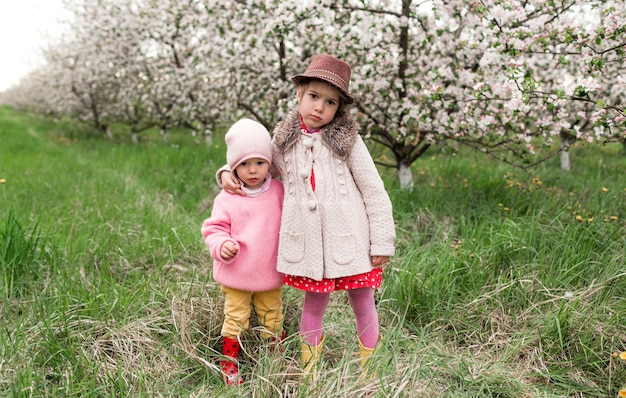 Duas meninas com roupas brilhantes e um chapéu se abraçam em um jardim florido. humor de primavera.