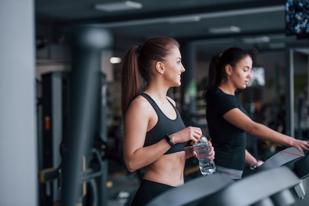 Duas meninas com roupas esportivas estão juntas no ginásio na esteira.