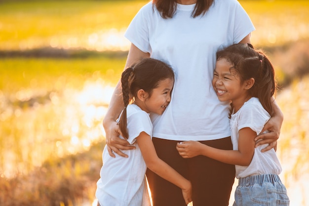 Duas meninas criança asiática, abraçando sua mãe e se divertindo para brincar com a mãe no arrozal