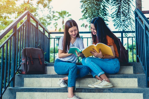 Duas meninas de beleza asiáticas lendo e tutoria livros para exame final juntos
