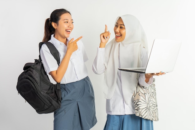 Foto duas meninas de escola secundária vocacional conversando carregando bolsas enquanto usam um laptop em um fundo branco